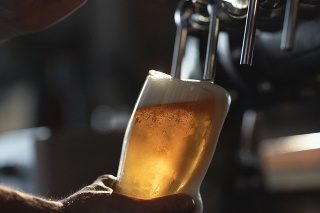 Fresh beer filling the glass directly from the tap.  With extra foam spilling over glass.