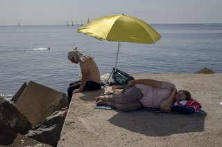 Na snímke žena spí pod slnečníkom na vlnolame pri Stredozemnom mori v španielskej Barcelone.