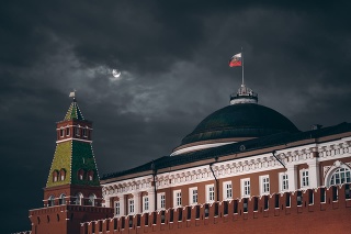 Night shot: Kremlin Moscow Dome of Senate building, a red Kremlin wall, flag of Russia with the emblem on it; sinister dark sky with a moon partly closed by the clouds
