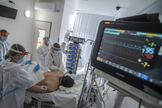 Doktori a zdravotné sestry v ochrannom oblečení sa starajú o covid pacienta napojeného na ventilátor na jednotke intenzívnej starostlivosti.