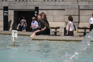 Ľudia sedia s nohami vo fontáne na námestí Trafalgar Square v Londýne.