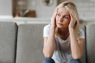 Sad caucasian senior woman wearing casual clothes sits on couch at home alone feels unhappy because of headache, stress, illness or bad news, she needs rest and sleep