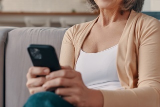 Beautiful senior woman in casual clothing using her smart phone while sitting on the sofa at home