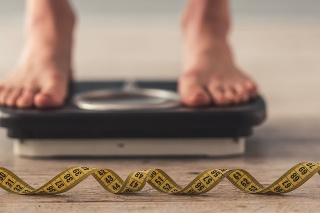Cropped image of woman feet standing on weigh scales, on gray background. A tape measure in the foreground