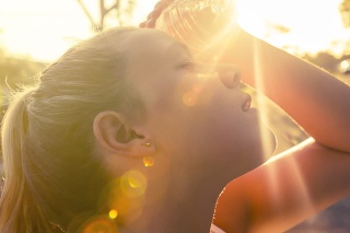 Woman using water bottle to cool down. Fitness and wellbeing concept with female athlete cooling down on a city street. She is holding a water bottle to her head to cool down. The sun is low creating long shadows and some lens flare. Copy space