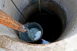 an iron bucket on a wooden stick with water at the depth of an old round well