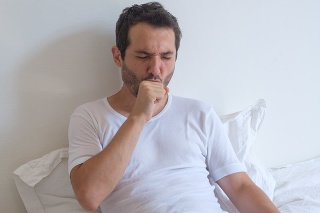 Sick man lying on bed and coughing a lot