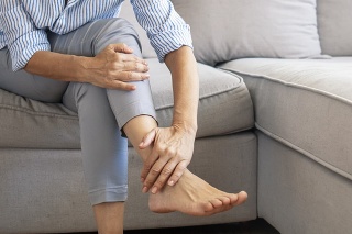 Closeup young woman feeling pain in her foot at home. Healthcare and medical concept. Tired and aching female feet after walking. Woman with feet intense pain sitting on a couch at home.