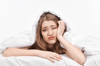 woman at the edge of her bed with negative expression feeling sick and looking at camera displeased.