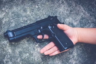 Gun in the hands of a children on a gray background.