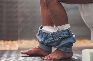 Cropped image of handsome Afro American man sitting on toilet. His jeans is hanging on his legs