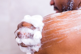 brazilian man washing body with shower sponge in white bathroom.