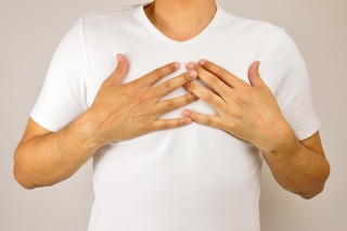 man with both hands on breast because of hard breathing and angina pectoris on grey background