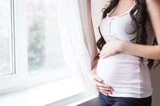 Pregnant woman standing by the window. Close up