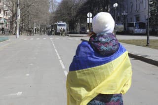Na archívnej snímke z 19. marca žena s ukrajinskou vlajkou stojí  pred ruskými vojakmi počas zhromaždenia proti ruskej okupácii v ukrajinskom meste Cherson.