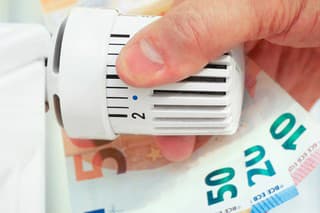 Hand on the heating thermostat with money bills, heating costs concept
