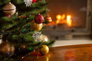 Closeup image of golden and red baubles on Christmas tree in front of burning fireplace. Beautiful Christmas background
