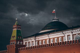 Night shot: Kremlin Moscow Dome of Senate building, a red Kremlin wall, flag of Russia with the emblem on it; sinister dark sky with a moon partly closed by the clouds