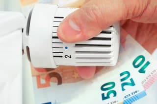 Hand on the heating thermostat with money bills, heating costs concept