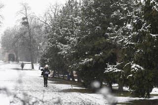 Ľudia kráčajú po chodníku počas sneženia v Košiciach.