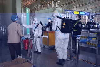 Cestujúci v ochranných výstrojoch na letisku v Pekingu.