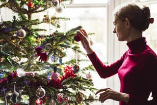 Side view of Caucasian female British teenager hanging red bauble on traditional real Christmas tree