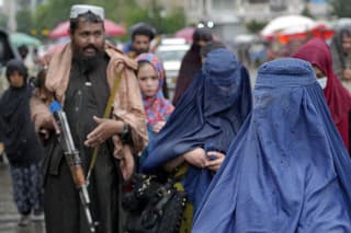 Ženy sa v utorok 3. mája 2022 prechádzajú starým trhom, zatiaľ čo bojovník Talibanu stojí na stráži v meste Kábul v Afganistane.