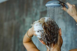 Back view of a woman washing her hair with a shampoo in bathroom. Copy space.