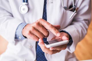 Unrecognizable senior male doctor with smartphone at the office, text messaging.
