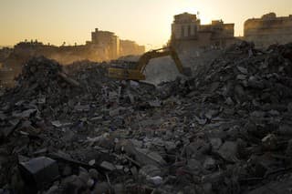 Báger rýpe v troskách zničených budov po ničivom zemetrasení v meste Iskenderun na juhu Turecka.