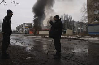 Miestni obyvatelia sa rozprávajú a v pozadí stúpa dym z horiacej budovy po ostreľovaní ruskej armády v meste Časiv Jar v Doneckej oblasti.