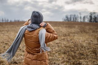 Wind and cold weather. Woman wearing coat, scarf and knit hat outdoors. Female person walks in nature