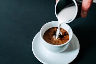 Pouring milk in black coffee. Isolated background.