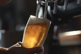Fresh beer filling the glass directly from the tap.  With extra foam spilling over glass.