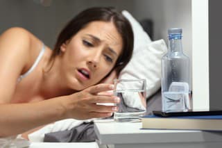 Dehydrated woman reaching a glass of water on the bed in the night at home