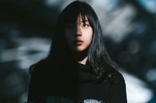 A portrait of a young Asian woman while half of her face is lit by the sun and the other half is in the shadow.