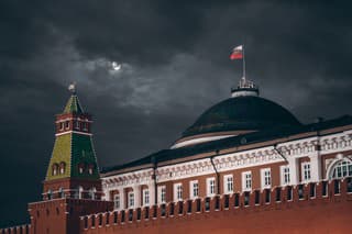 Night shot: Kremlin Moscow Dome of Senate building, a red Kremlin wall, flag of Russia with the emblem on it; sinister dark sky with a moon partly closed by the clouds