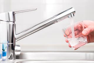 Filling glass with tap water. Modern faucet and sink in home kitchen. Man pouring fresh drink to cup.