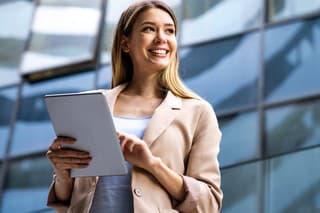 Successful attractive businesswoman using a digital tablet while standing in front of business building. Business people work concept
