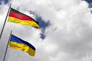 Three international flags of Ukranie, Germany and European Union against the blue and cloudy sky with a blank for copy space