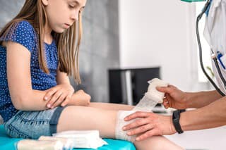 Medical female doctor bandaging young girl knee at the hospital
