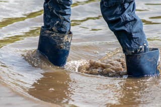 Young boy with short blue trowsers wading with wet socks and wet boots through high tide after a floodwater has broken the dike and overflown the lands behind
