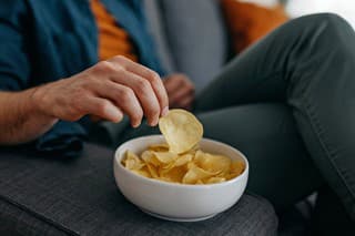 Young unrecognizable young  caucasian  man at home, sitting on sofa and taking a potato chip from a bowl placed on a sofa