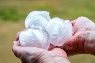 An unrecognizable women is showing a small group of very big ice hailstones just fallen from the sky with violence, holding in her hands. This picture was taken in selective focus on ice, white color sphere shape, impressive hail size has done a lot of damage in march in end of winter season outdoor.