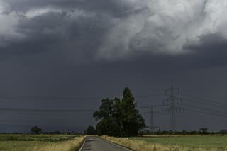 An empty country road and cultivated fields with a storm and gray sky on the horizon