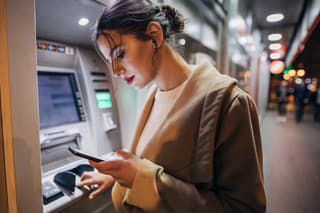 One young beautiful young teenage girl using ATM machine and smart phone in the city