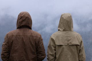 Man and woman in raincoats enjoying mountain landscape under rain, back view