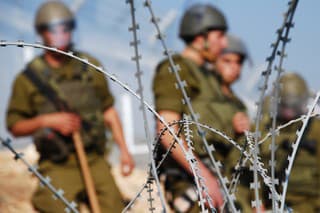 Four Israeli soldiers stand behind razor wire near the Palestinian village of Bil'in in the West Bank