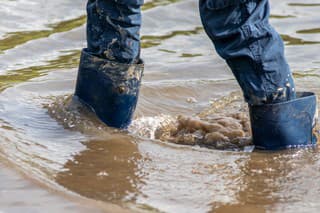 Young boy with short blue trowsers wading with wet socks and wet boots through high tide after a floodwater has broken the dike and overflown the lands behind