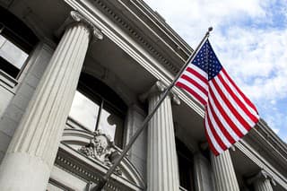 Stone granite official government building in city with American flag waving and flying in the wind, looking up, outside, judicial, freedom, civil courts, columns, criminal justice, law